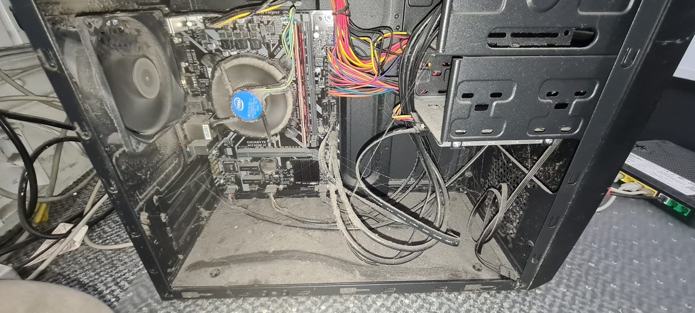 Inside a very dusty desktop PC: CPU cooler clogged with dust, cables furred up and a thick layer of dust on the case floor